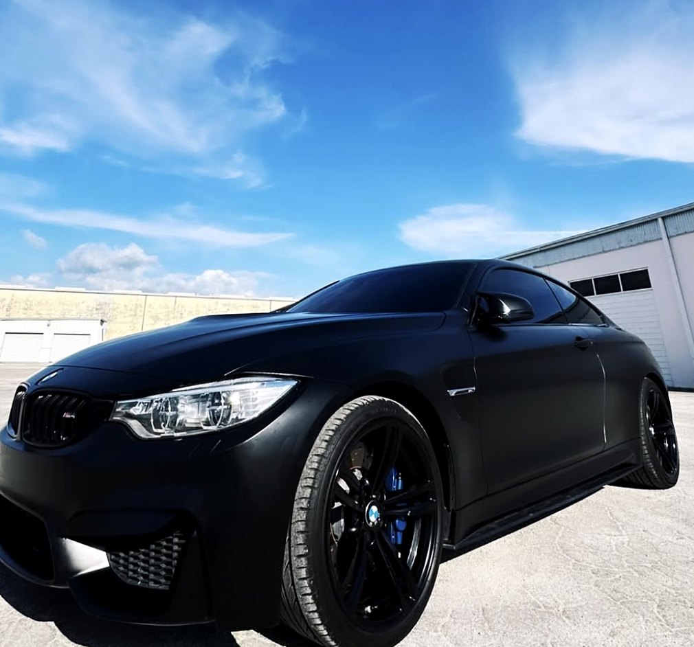 BMW M4 coupe wrapped in matte black vinyl with black wheels and blue brake calipers